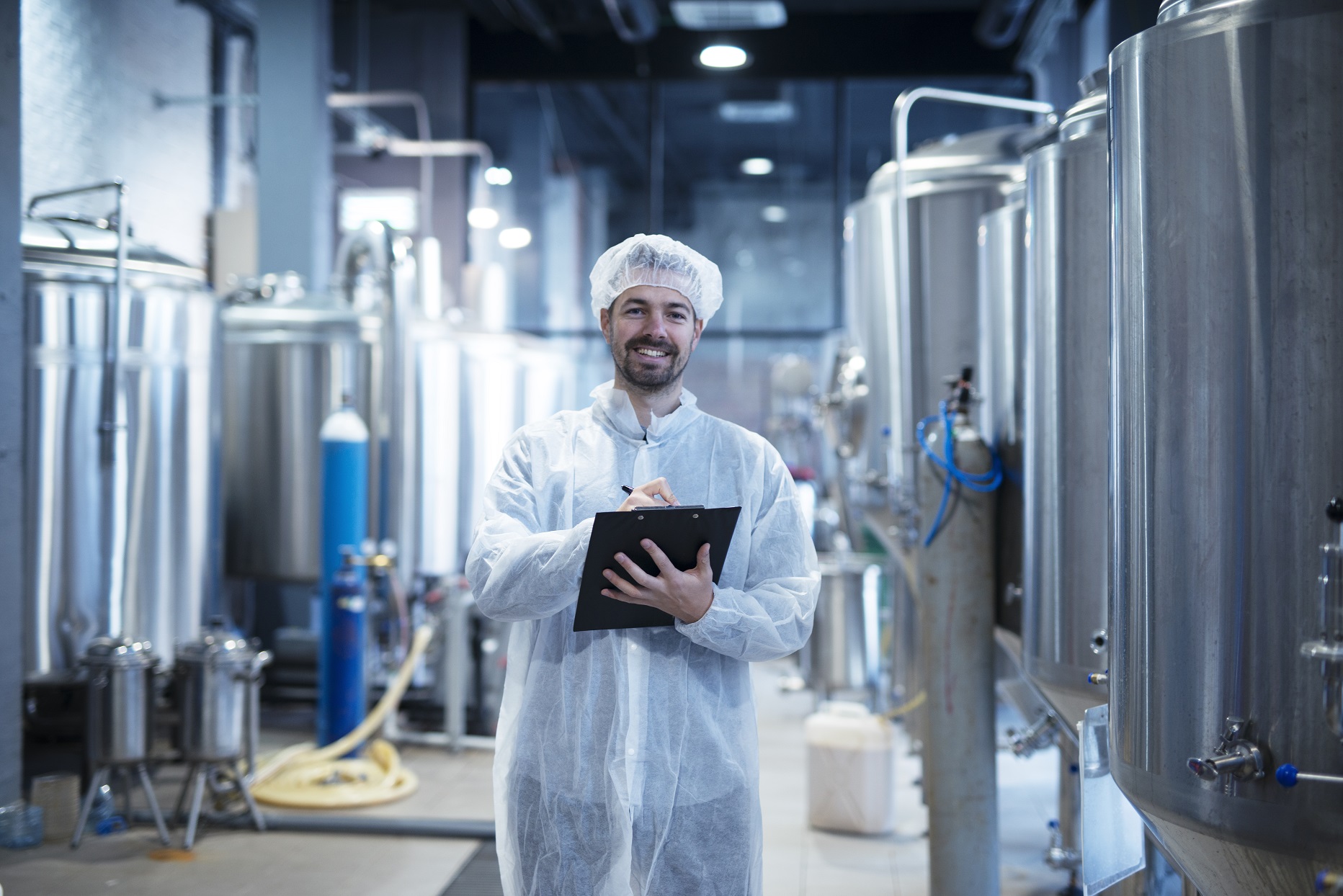 Food processing plant interior with positive smiling technologist holding checklist.